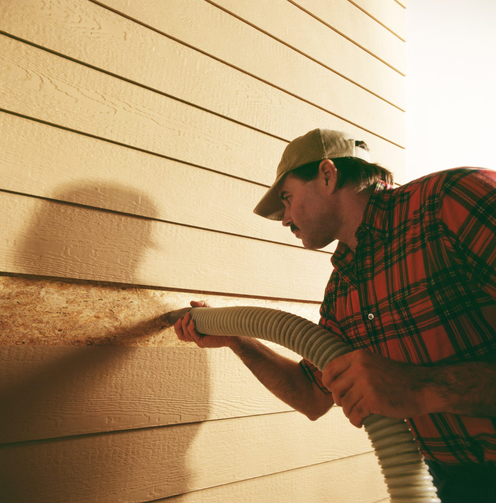 A technician adding retrofit insulation into the walls of a home